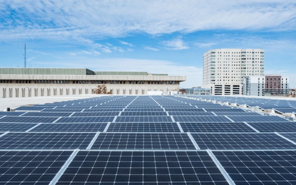 Panoramic view of a building rooftop filled with solar panels, with other building structures visible in the background.